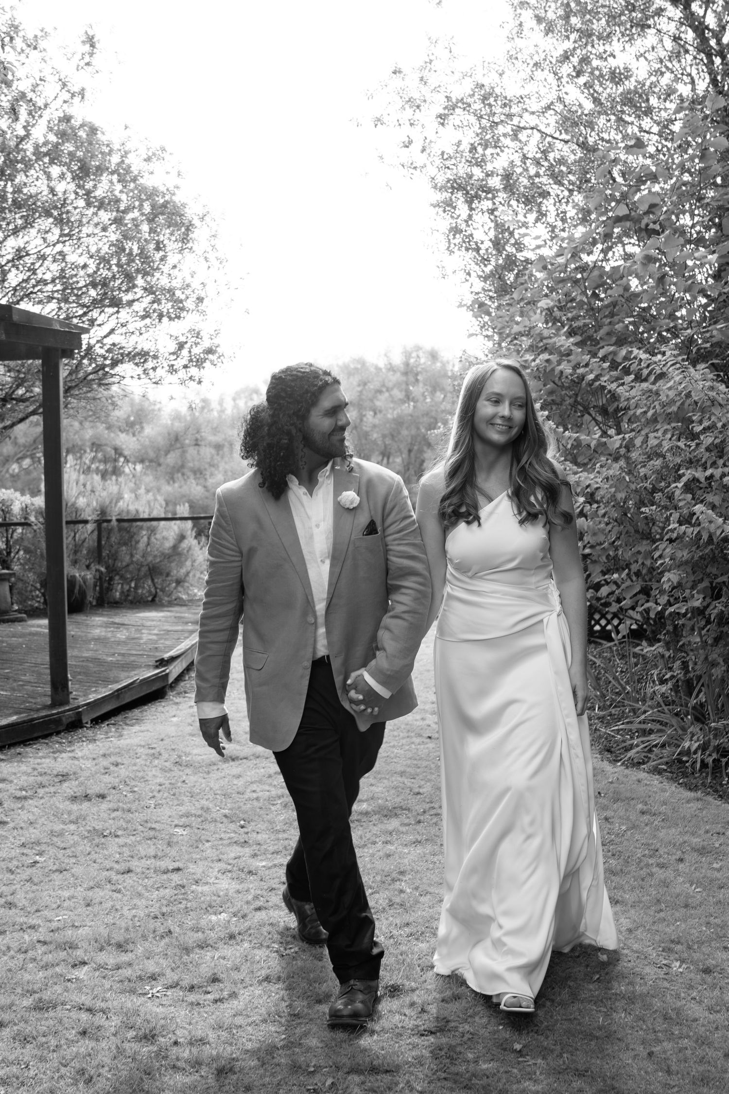 Black and white photo of a bride and groom holding hands and walking together outdoors on their wedding day.