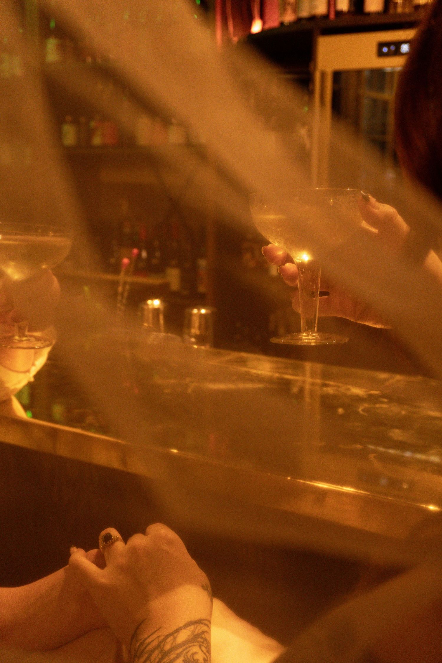 Moody bar scene with golden light rays, cocktails, and tattooed patrons in a dimly lit lounge.