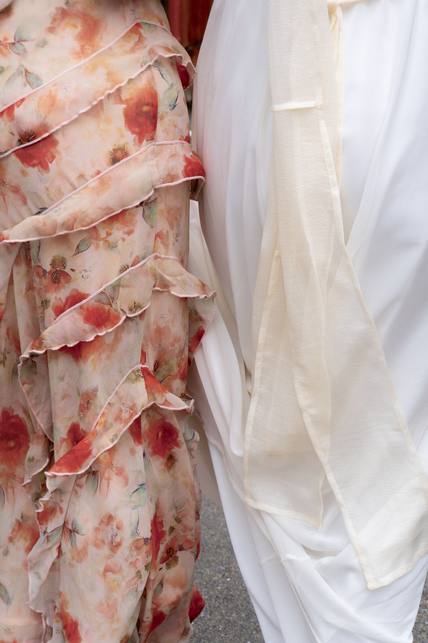 Close-up of a floral ruffled dress beside a white garment, showcasing elegant fabric textures and soft pastel tones.