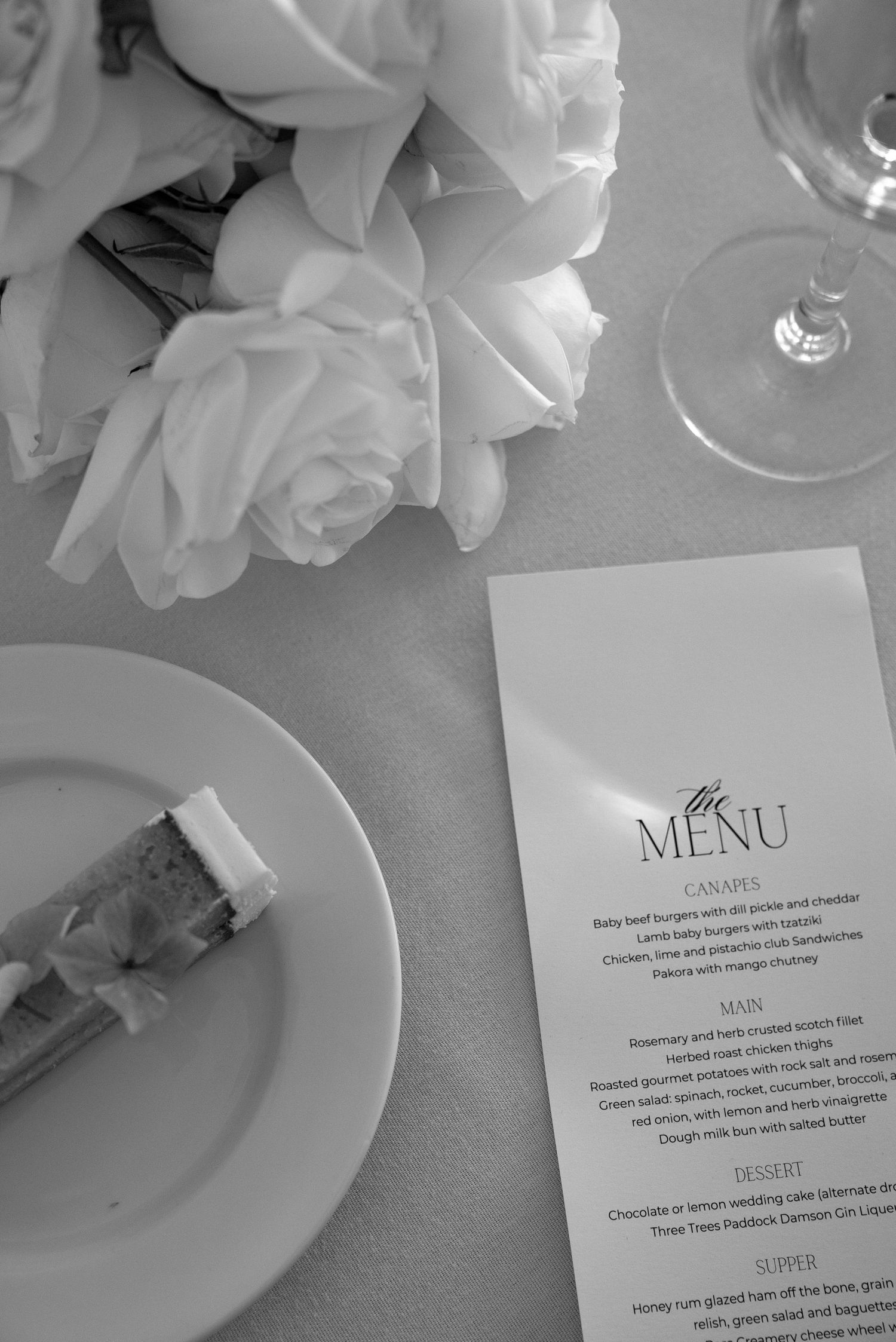 Elegant black and white wedding menu card on table with roses and wine glass.