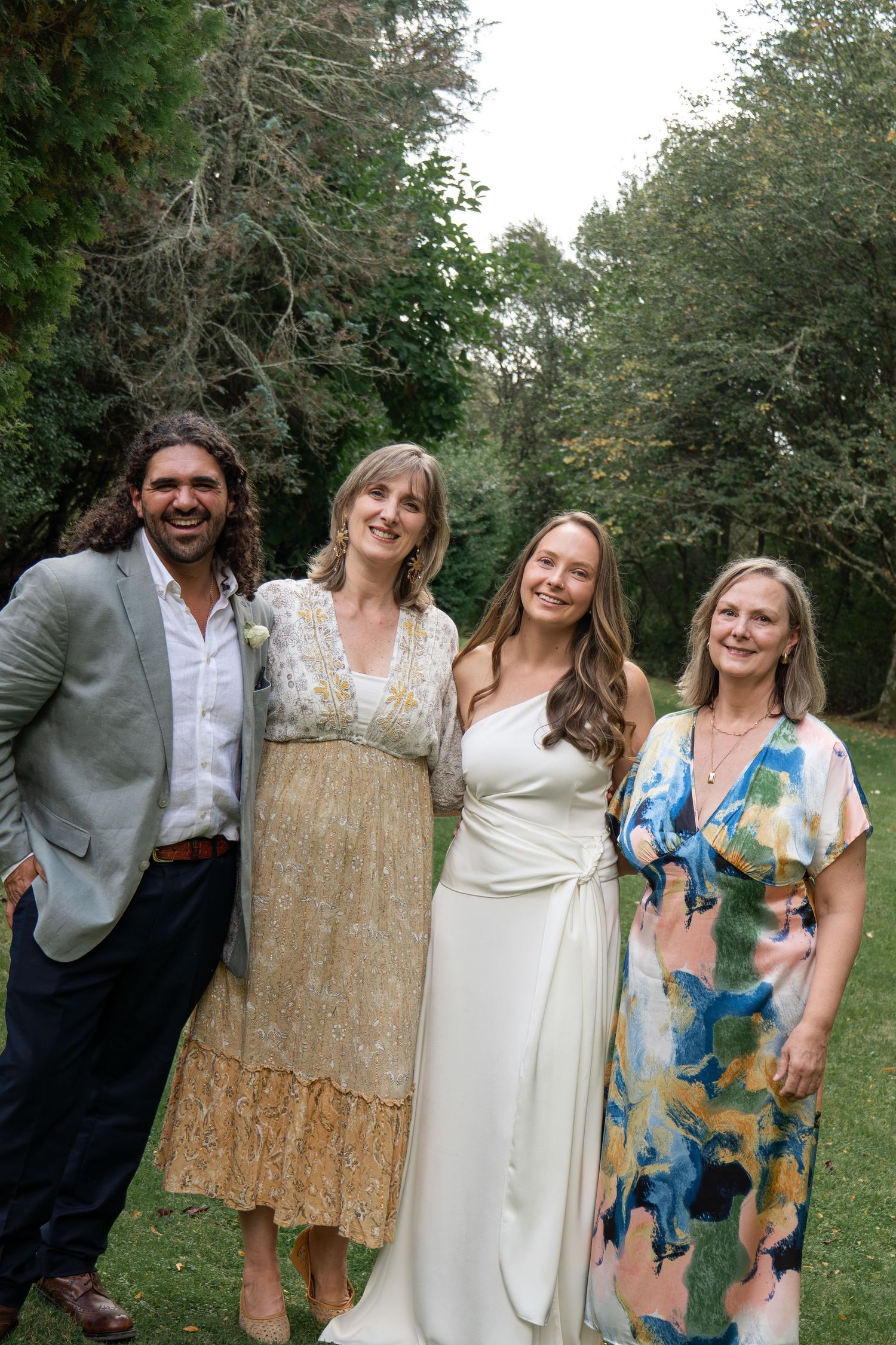 A bride in white dress poses with three guests outdoors at a garden wedding celebration.