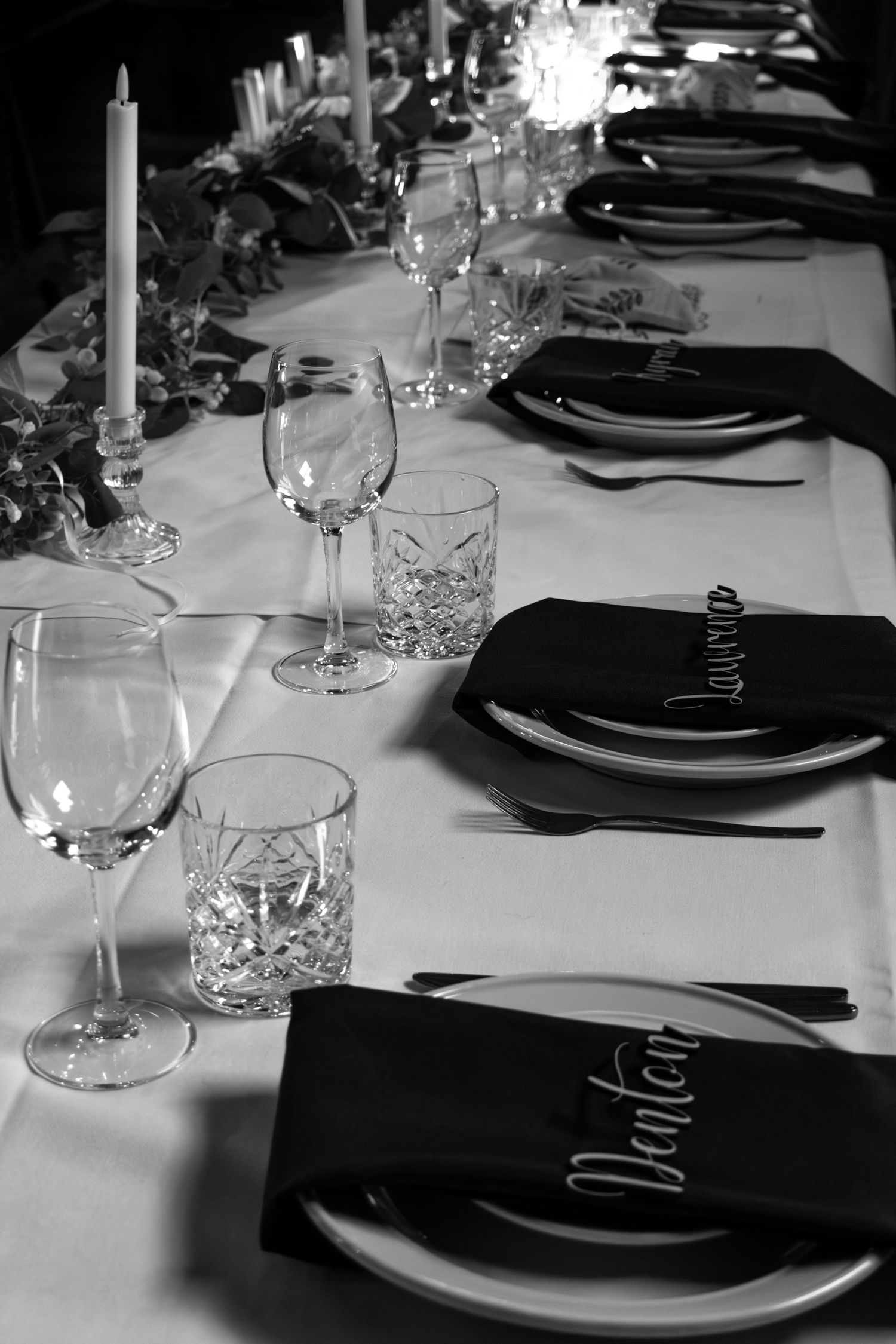 Elegant black and white formal dinner table setting with crystal glasses, dark napkins, name cards, and candles.