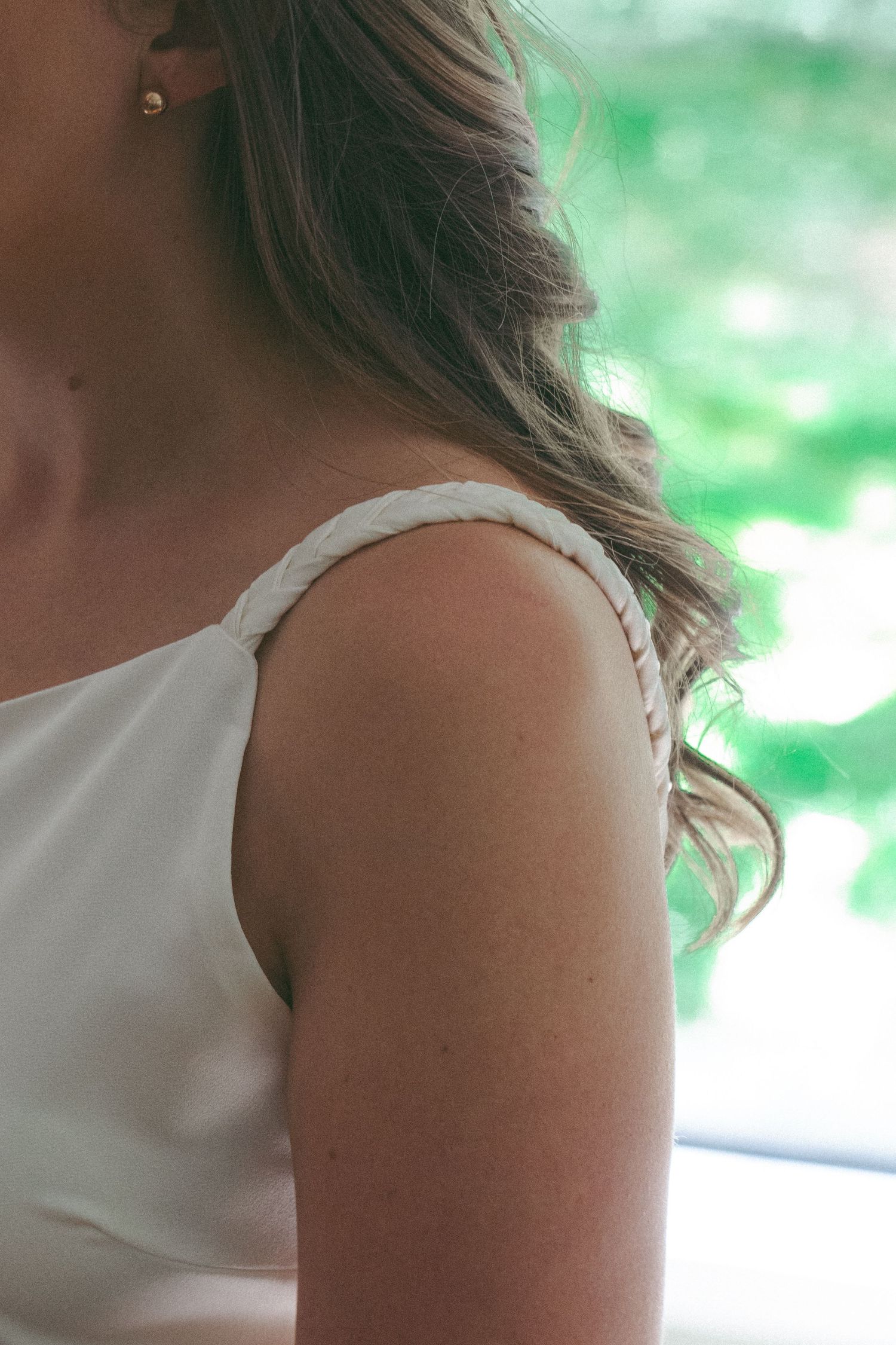 Close-up of a bride in a white dress with braided strap detail, showcasing elegant shoulder and hair styling.