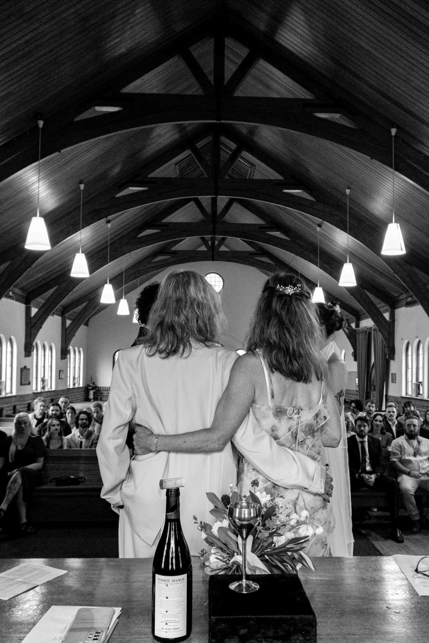 Black and white photo of two brides standing at church altar during wedding ceremony with guests seated in pews.