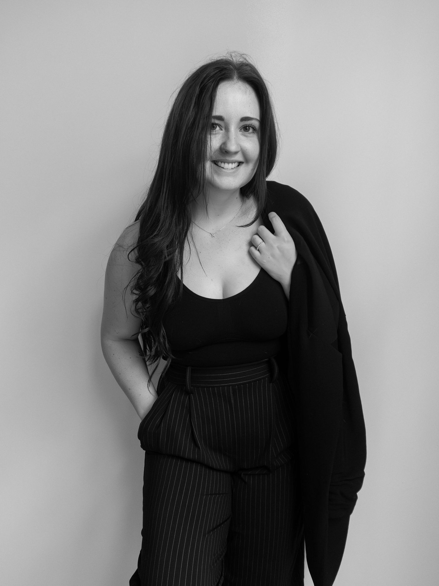 Black and white portrait of a smiling woman with long dark hair wearing a black outfit and blazer.