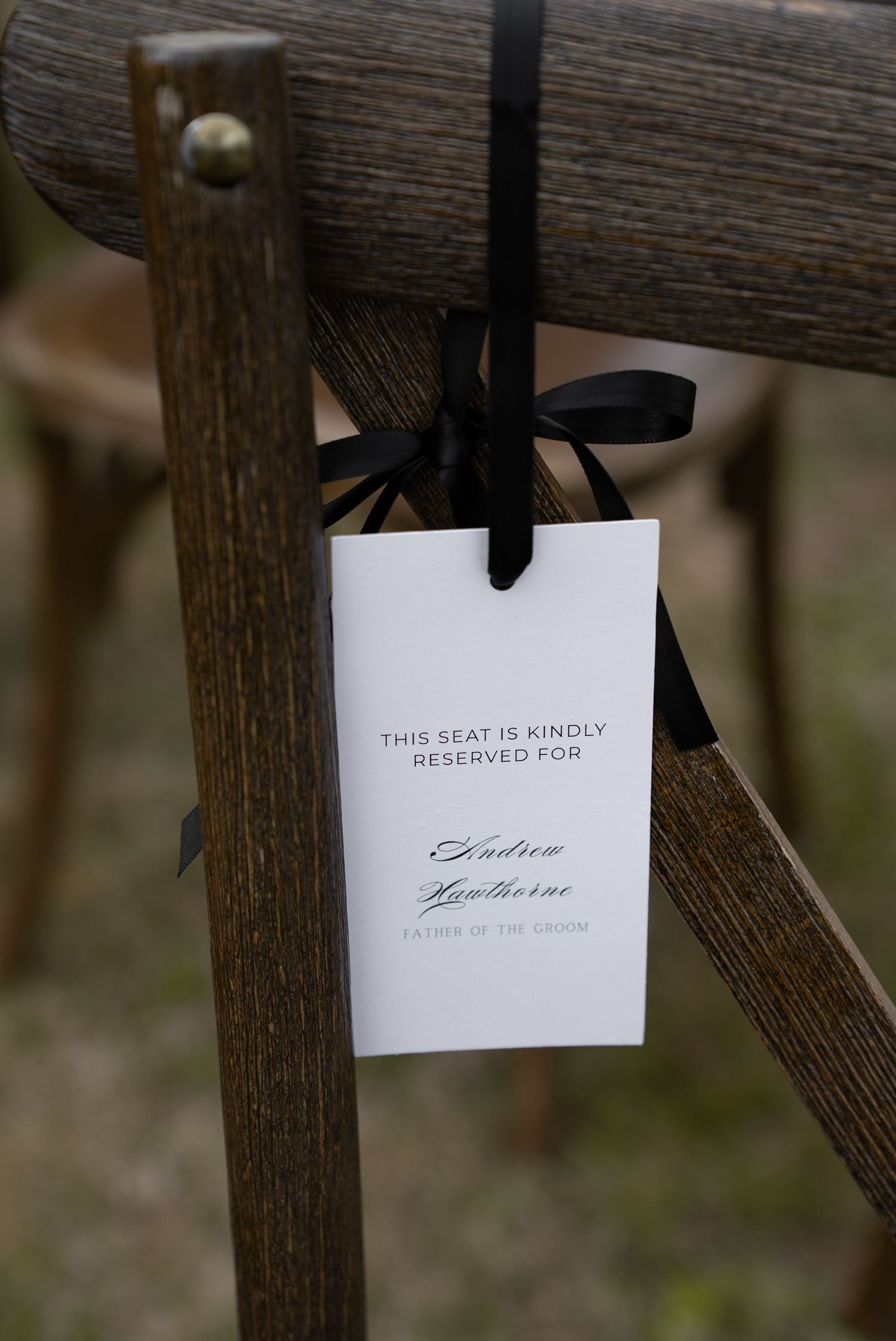 Elegant reserved seat card tied with black ribbon on wooden chair for Andrew Hawthorne, Father of the Groom.