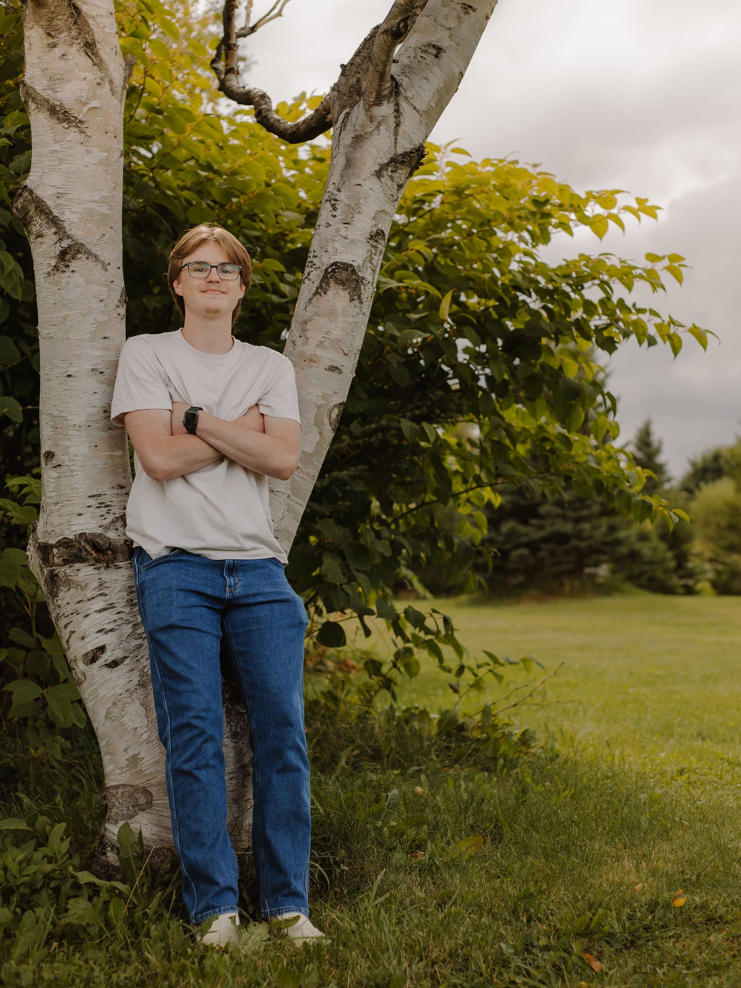 A young teen boy poses against a tree with a field behind him.