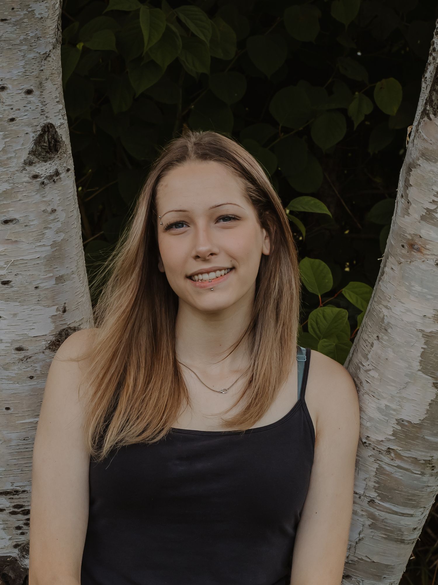 A teen girl poses against a tree.