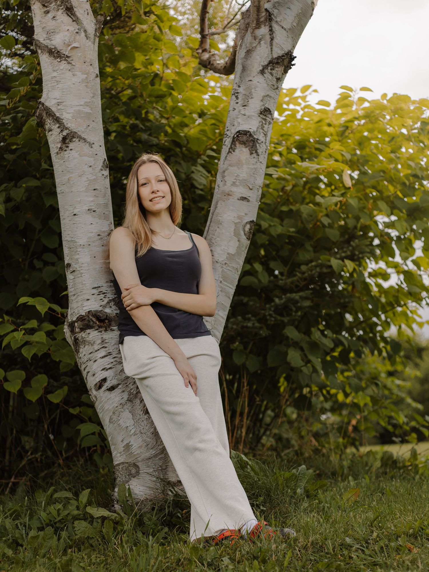 A teen girl poses against a tree.