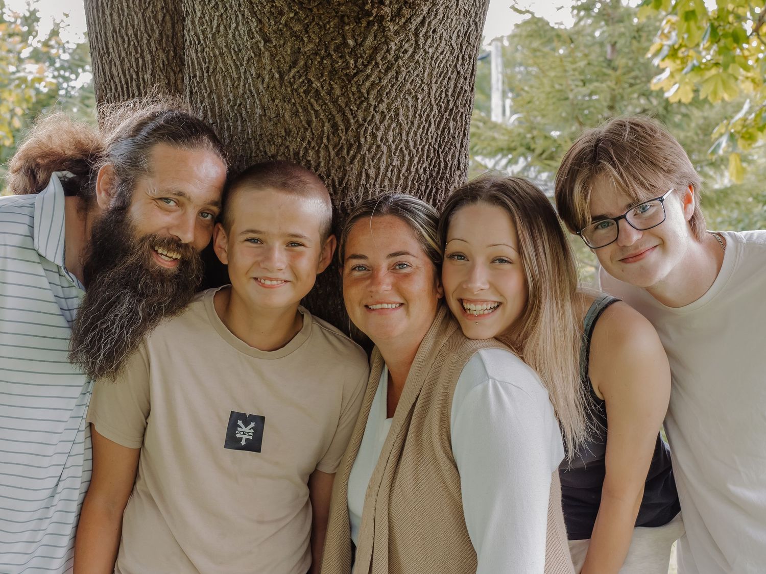 A family hugs together with a tree behind them.