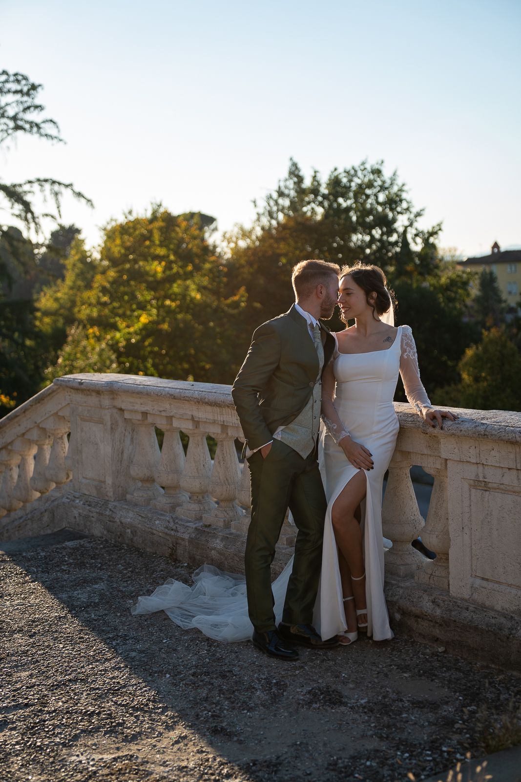 A couple shares a romantic moment at sunset on a stone balcony in a scenic outdoor setting.