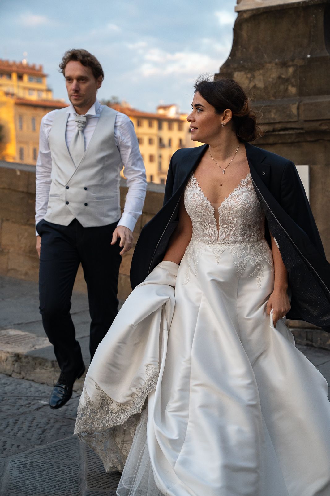 A couple in wedding attire poses together on a cobblestone street in Florence with historic buildings in the background.