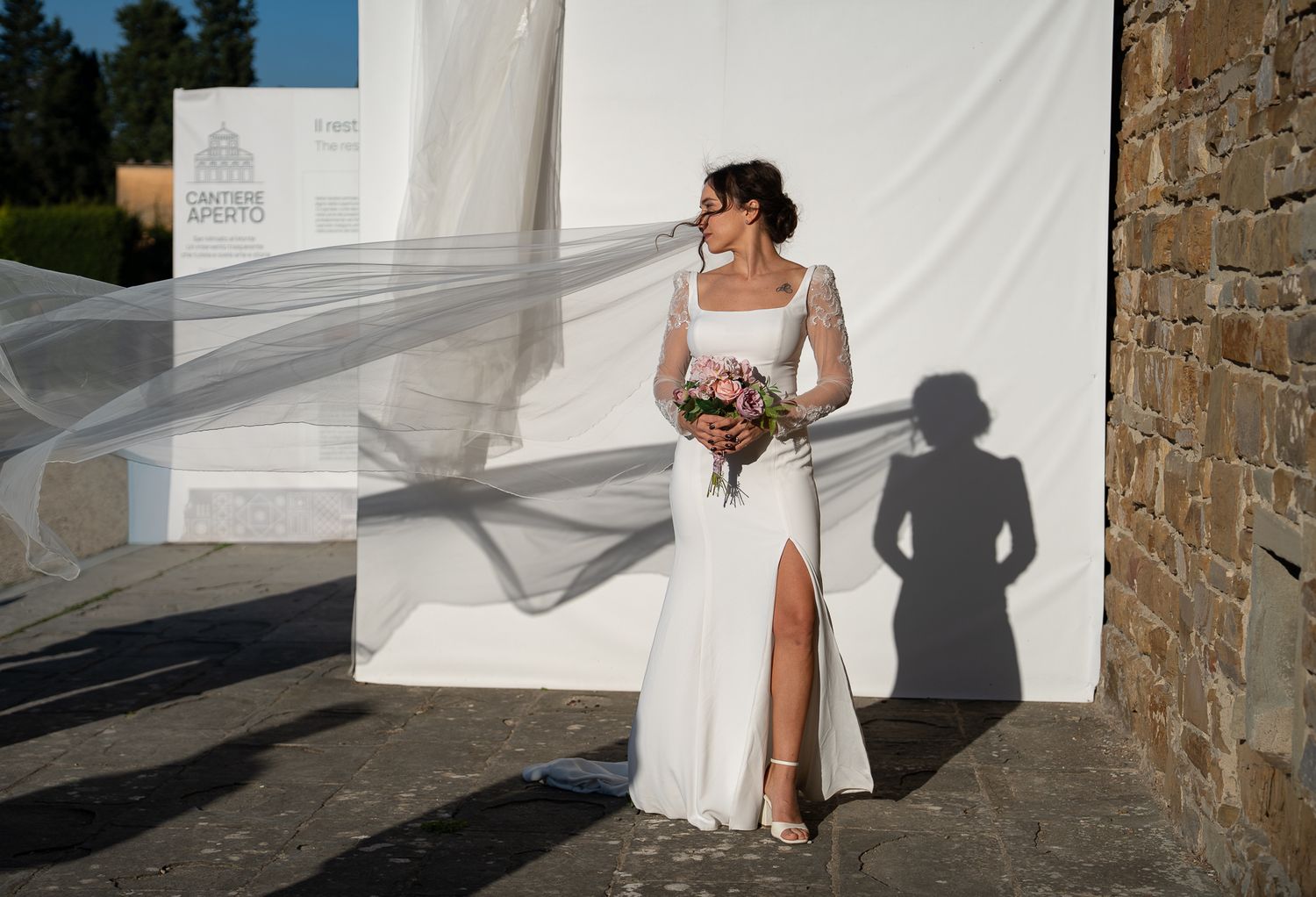 A wedding party stands against a white backdrop creating dramatic shadows on a sunny day.