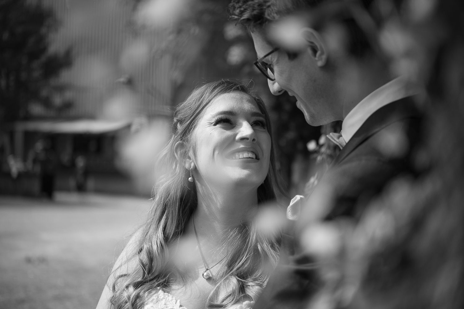 Black and white wedding photo of a bride gazing up at groom outdoors, capturing a romantic intimate moment.