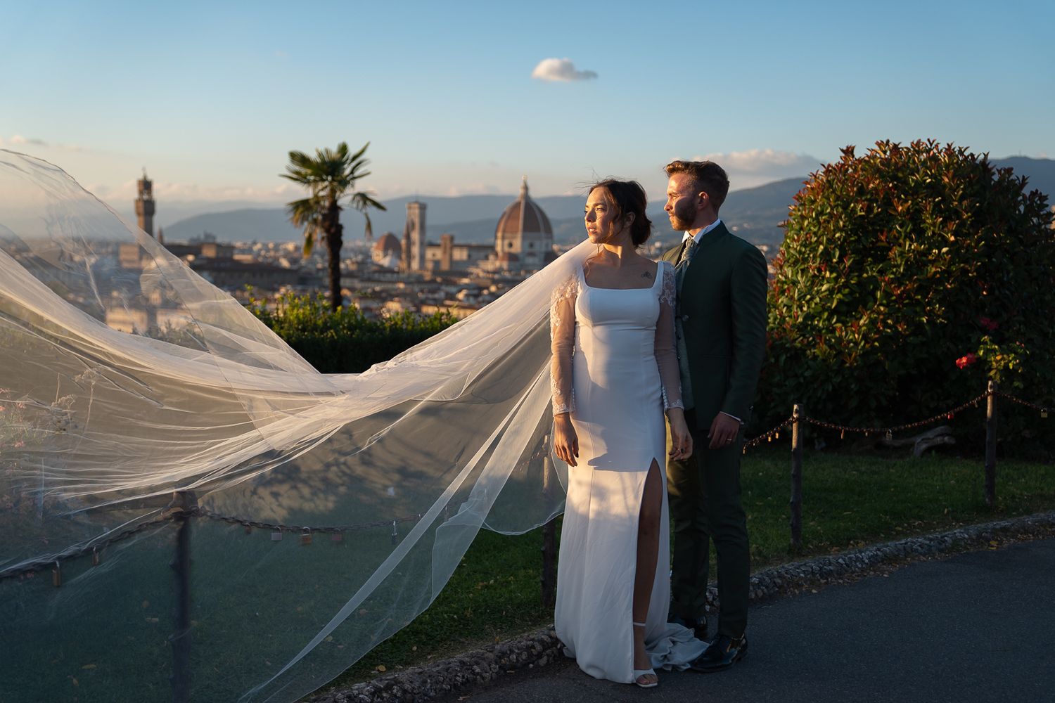 Long wedding veil billows in the wind against a scenic mountain landscape during sunset in Florence, Italy.