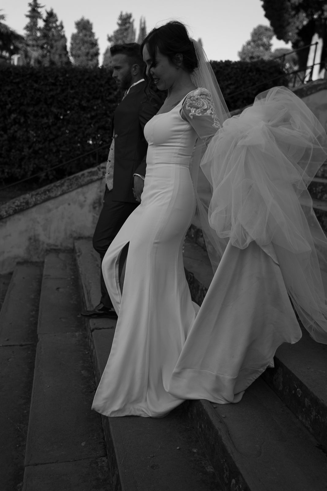 Black and white wedding photo showing couple on stone steps with flowing white dress and veil creating elegant silhouette in Florence, Italy