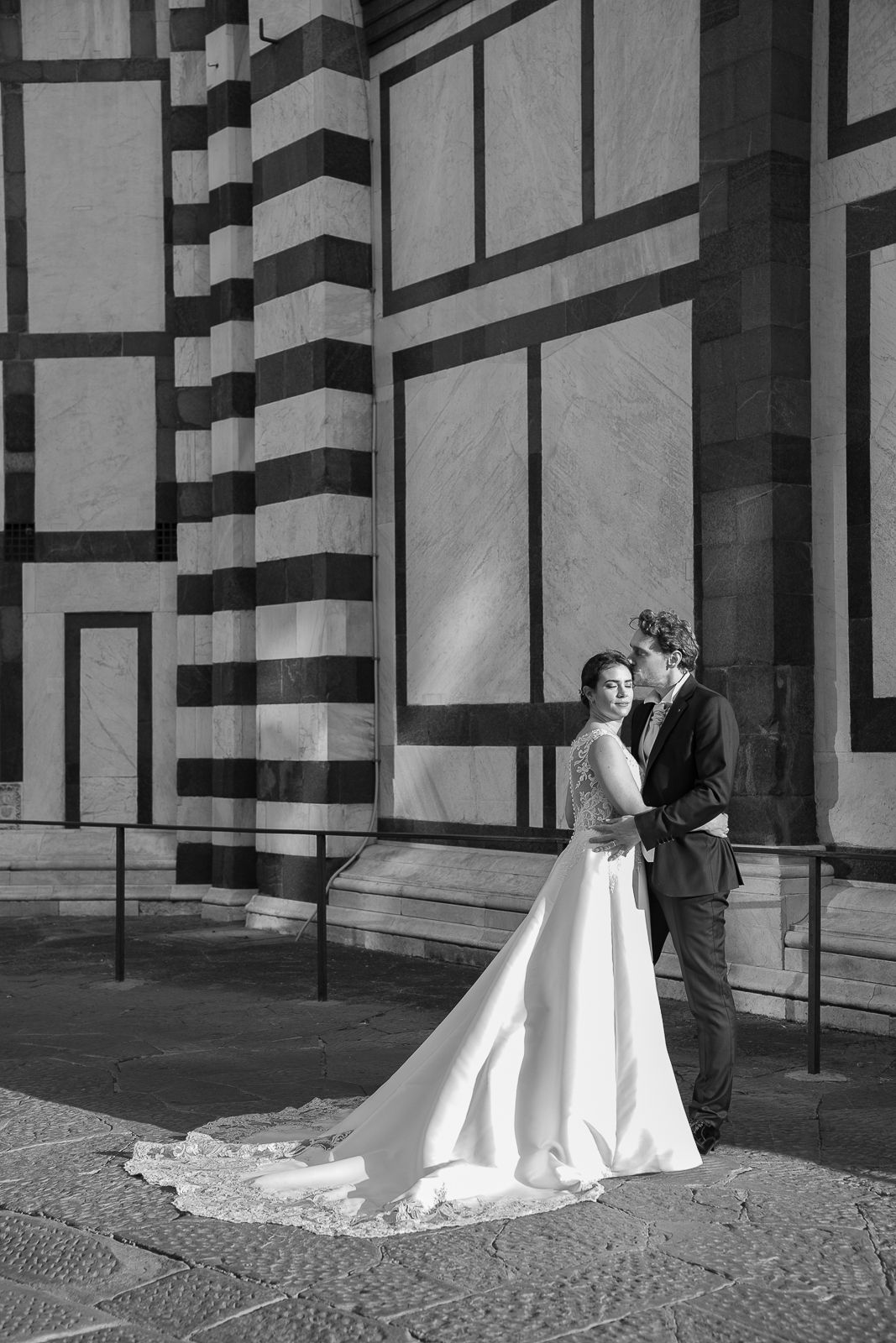 Black and white photo of a bride and groom embracing outside a marble cathedral in Florence, Italy.