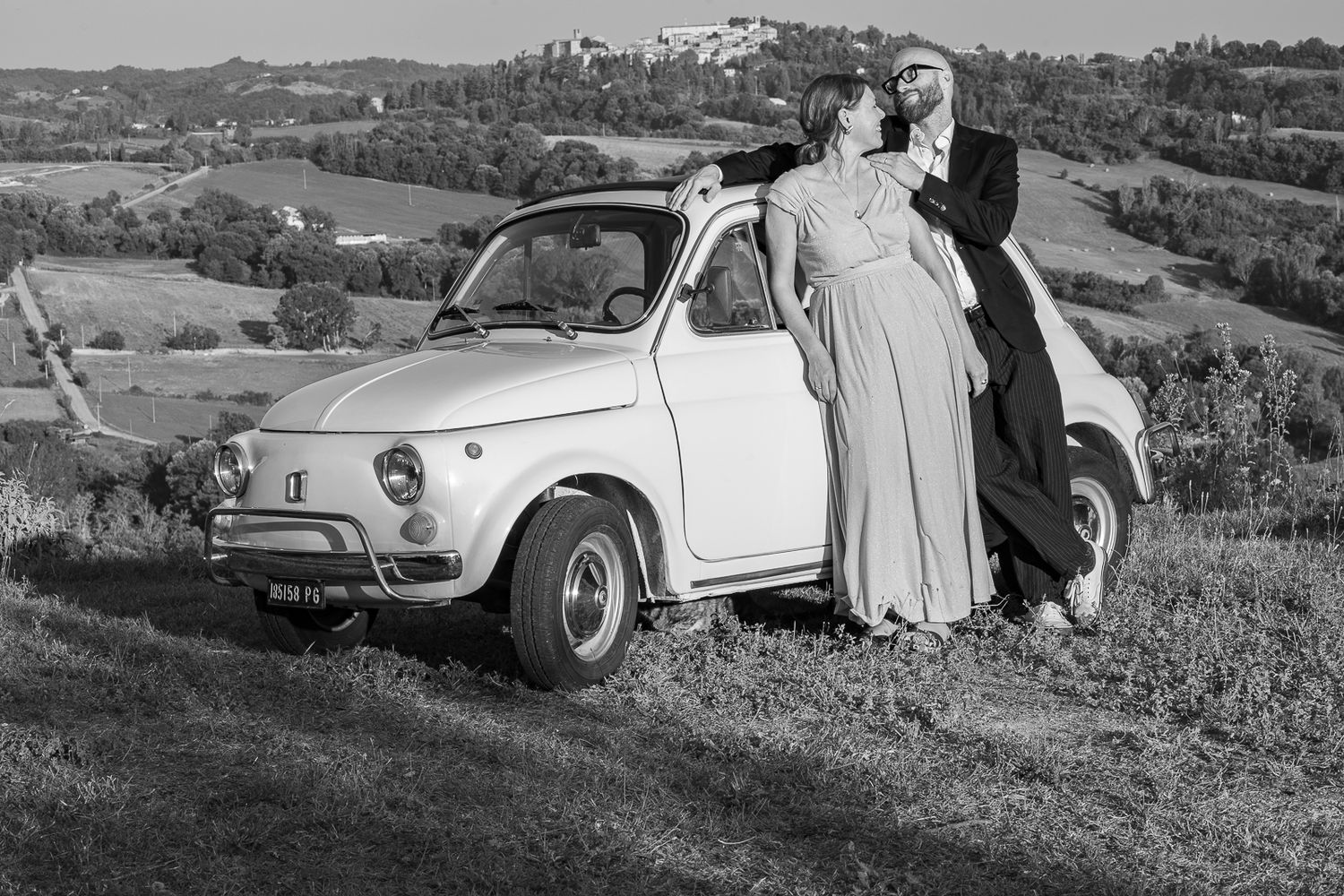 Classic car parked in scenic Italian countryside with cypress trees.