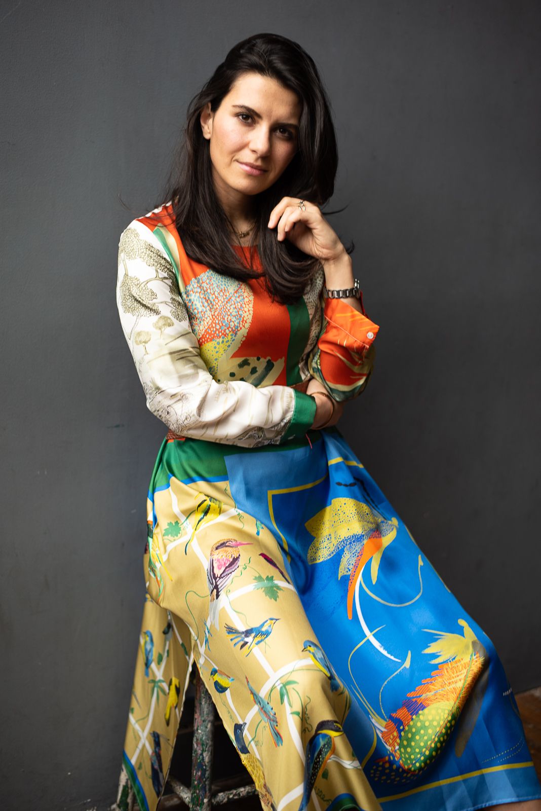 Fashion model wearing traditional Asian-inspired dress with vibrant yellow and blue floral pattern against dark background.