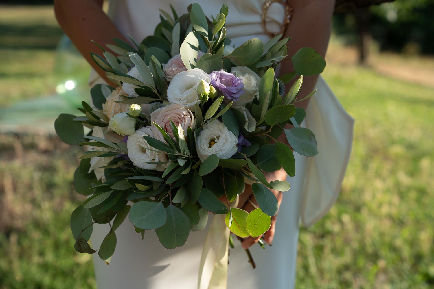 Bride in white dress holding a lush wedding bouquet with white roses, peonies, and eucalyptus greenery outdoors in Umbria, Italy