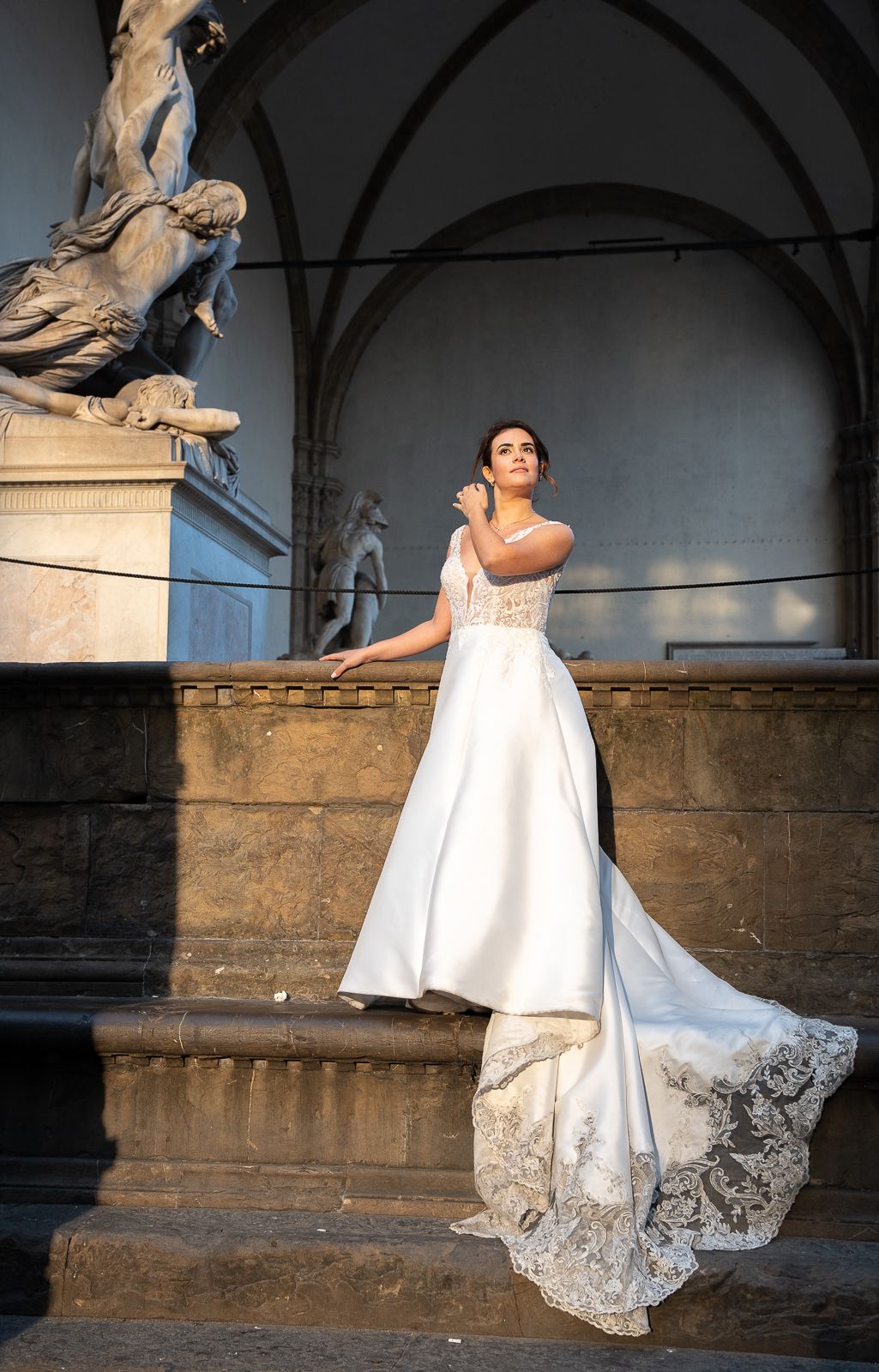 A bride in a flowing white dress with lace trim poses elegantly on stone steps in a series of artistic wedding photos.