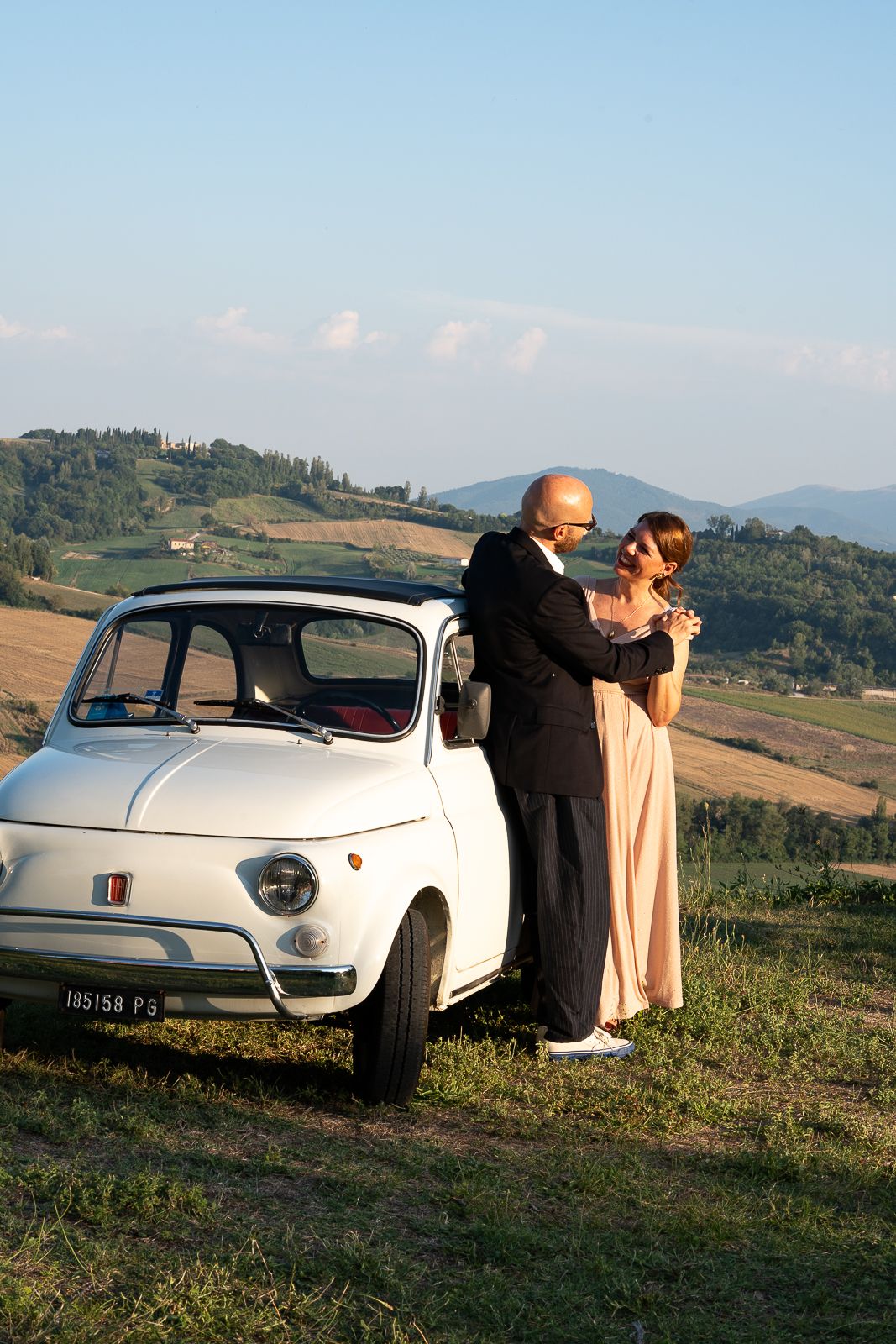 A vintage white Citroën DS parked on a hillside in the scenic Tuscan countryside at sunset.