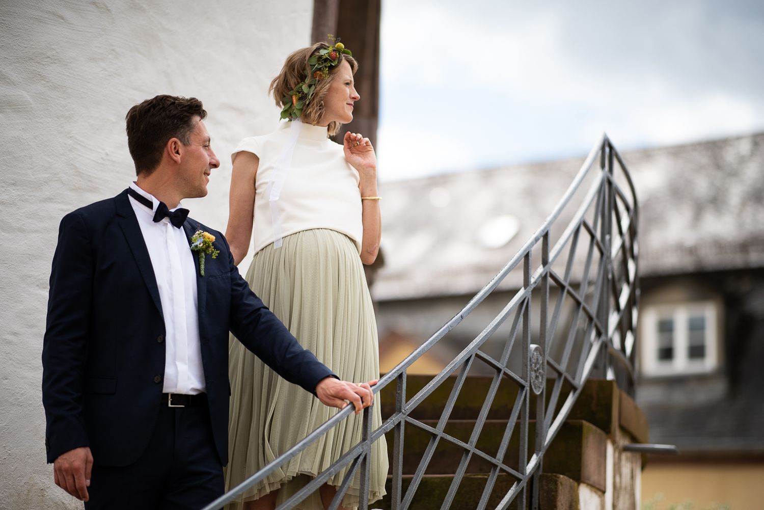 A couple in formal wedding attire share an intimate moment on a rooftop with city views in the background.