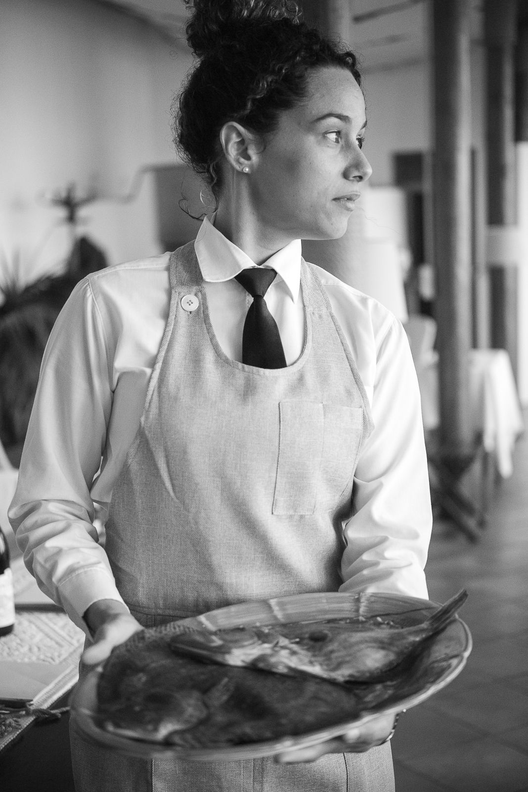 A server in formal attire and gray apron carrying a platter in black and white photography.