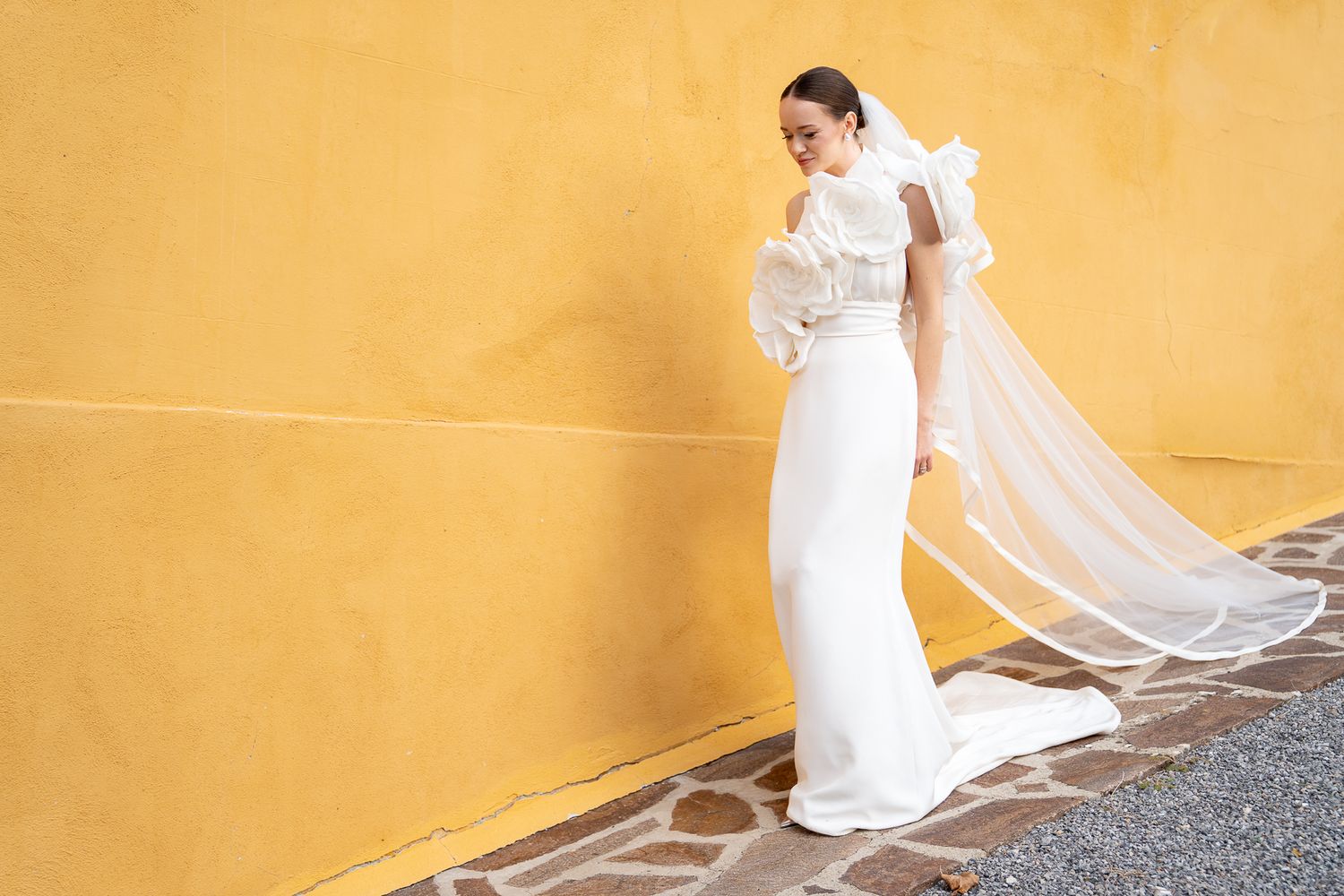 A person in a white dress walks past a yellow wall creating a flowing motion effect in the fabric.