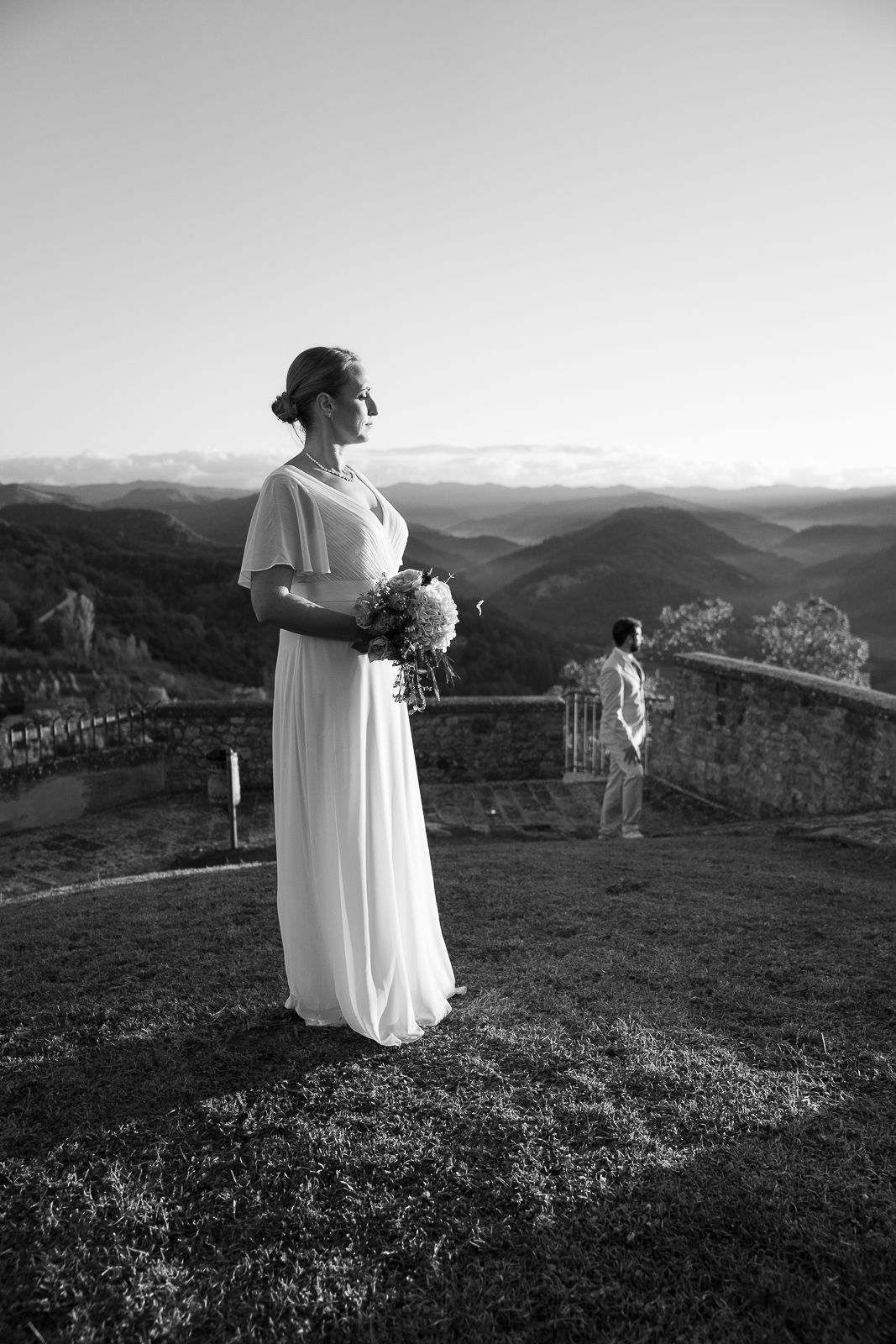 A person in white stands on a hilltop overlooking a mountainous landscape in black and white in Montone, Umbria, Italy