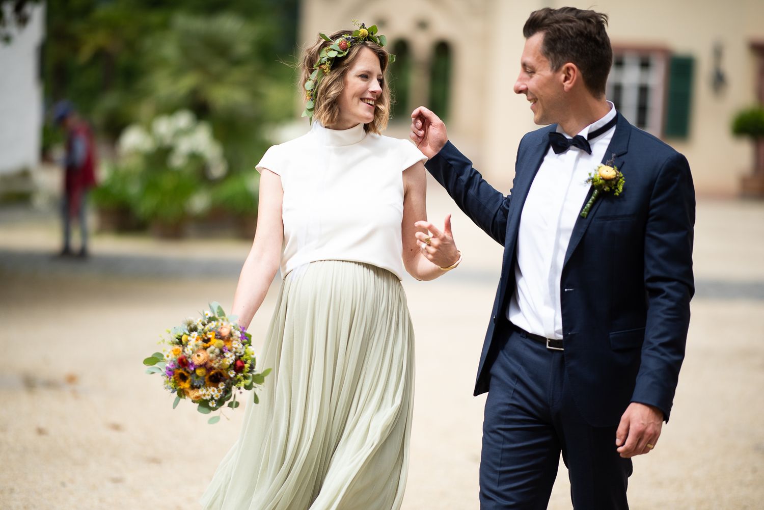 A couple in wedding attire walks together and laughs while holding a vibrant autumn bouquet.