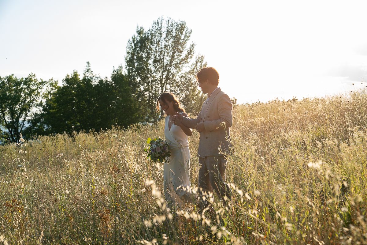 Couple holding hands in a sunlit wildflower meadow, bride holding bouquet, golden hour wedding photography outdoors by Friderika Wollweber