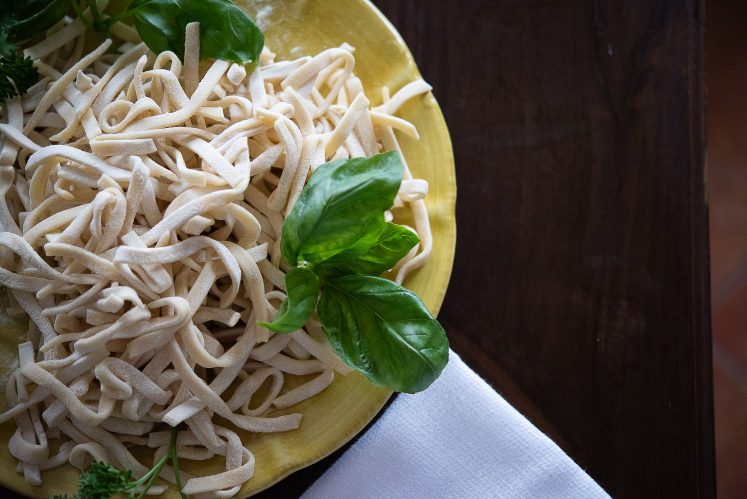 Bowl of white noodles garnished with fresh basil leaves on a yellow plate.