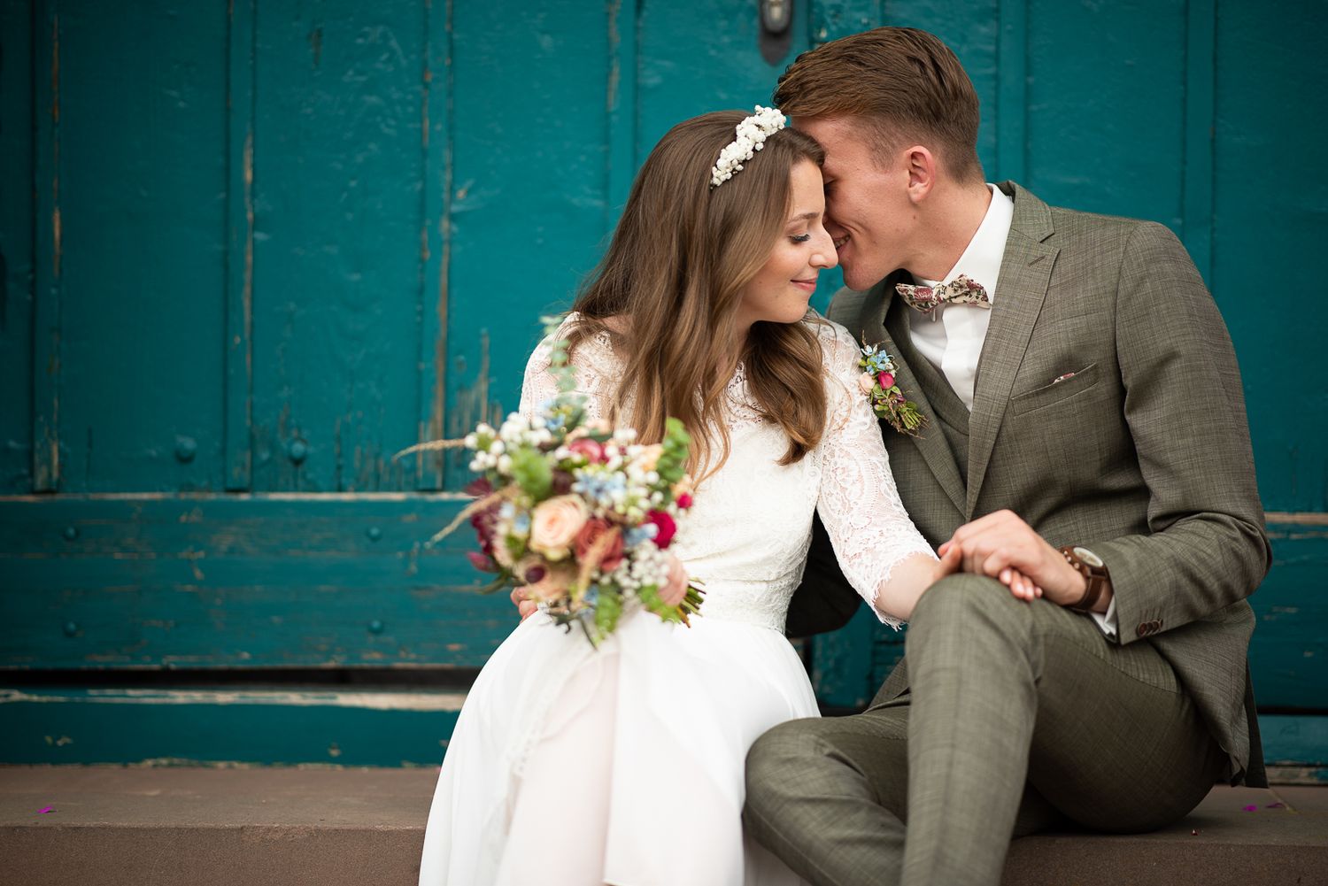 A romantic wedding couple share an intimate moment against a teal door background.
