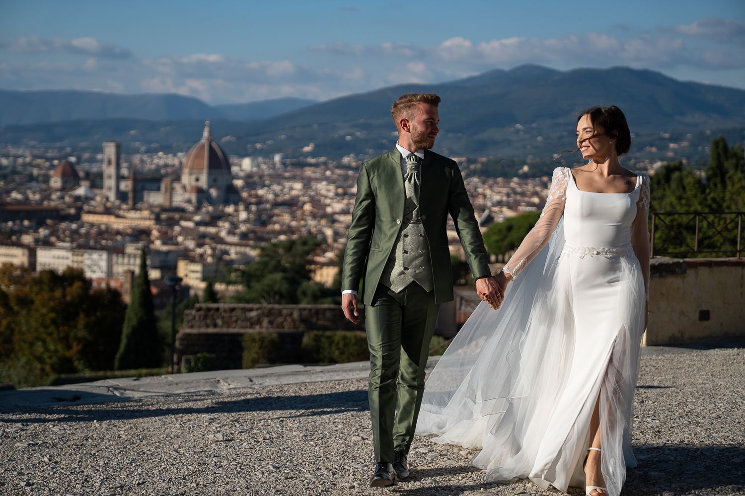 Wedding couple walks along scenic overlook with panoramic views of Florence, Italy and its iconic Duomo cathedral.