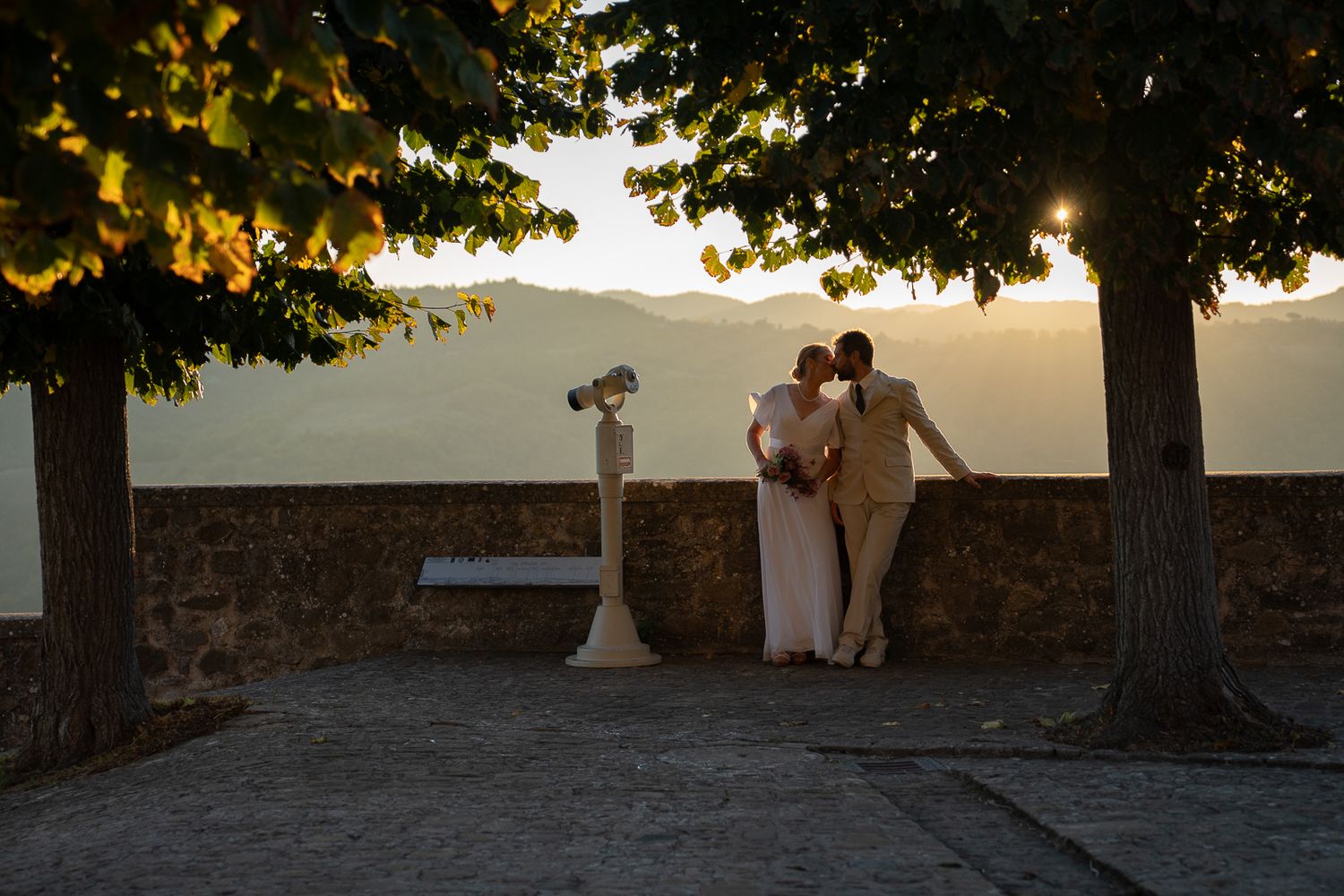A couple sits on a stone wall at sunset overlooking a scenic mountain landscape in Montone, Umbria, Italy