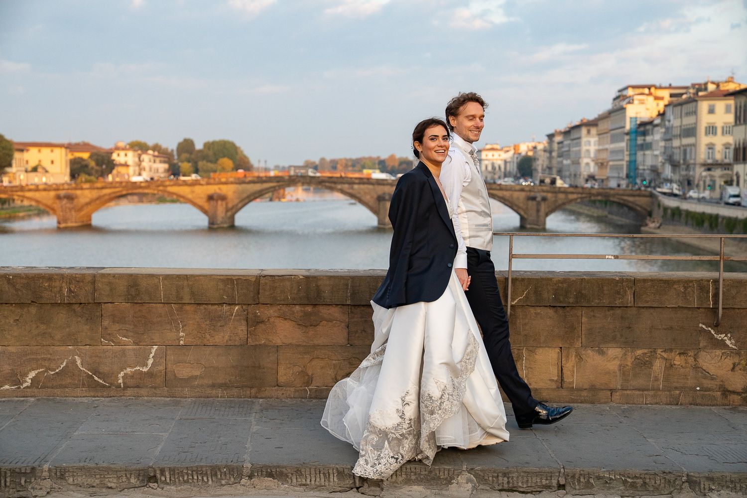 Couple poses together on a stone wall overlooking a coastal city during a sunset wedding photoshoot.