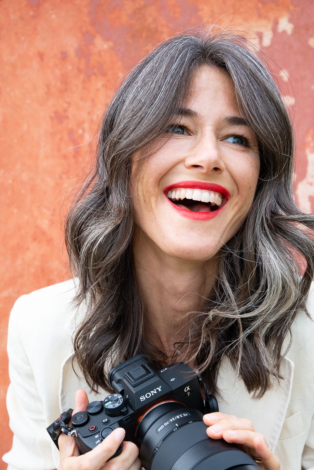 Sequence of candid expressions showing joyful moments while holding a Sony camera against an orange wall background.