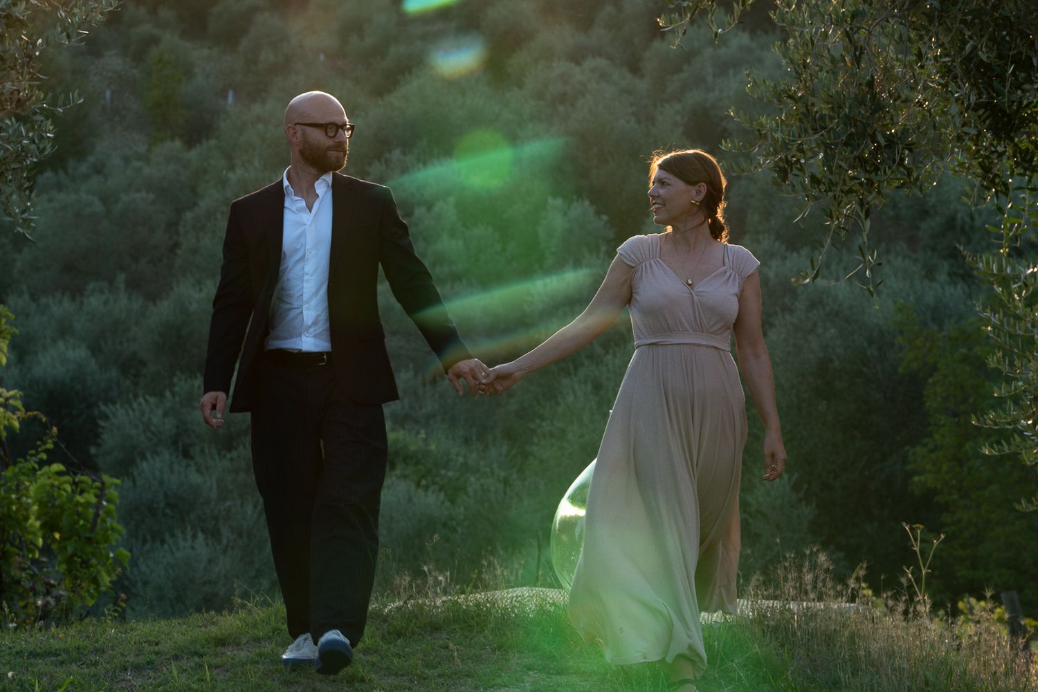 A couple walking hand in hand through a misty garden at sunset.