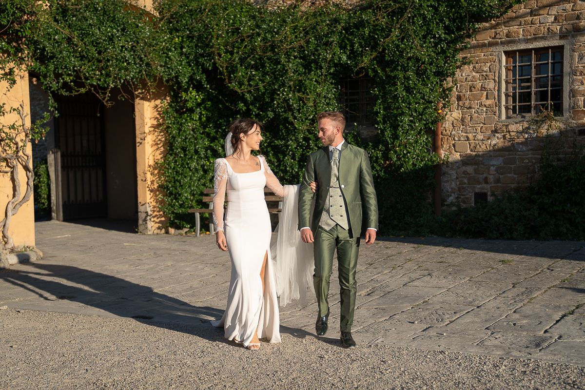 A couple walks together along a stone pathway outside a rustic building in warm evening light.