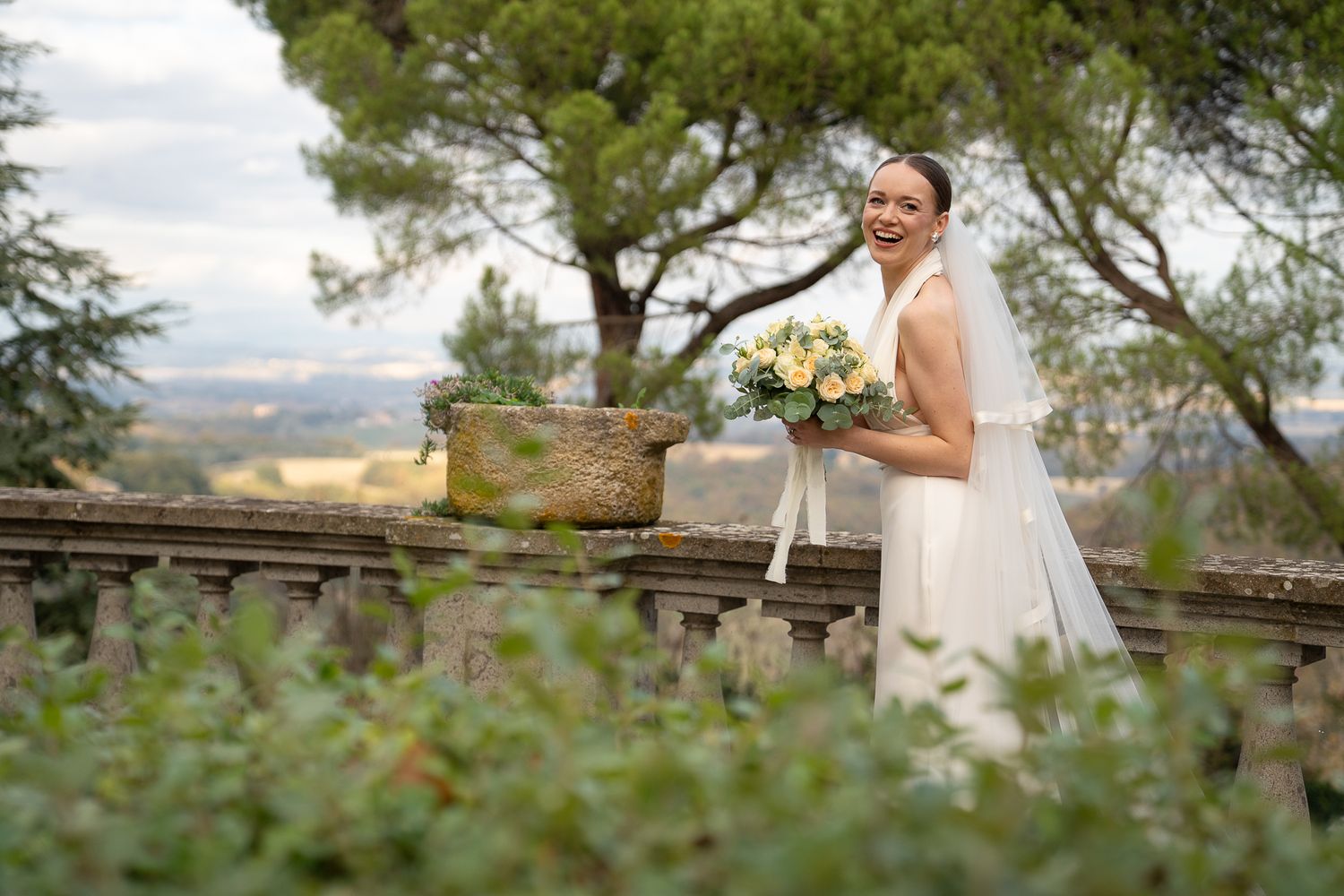 A bride in a white wedding dress poses in a scenic outdoor setting with mountains and trees in the background.