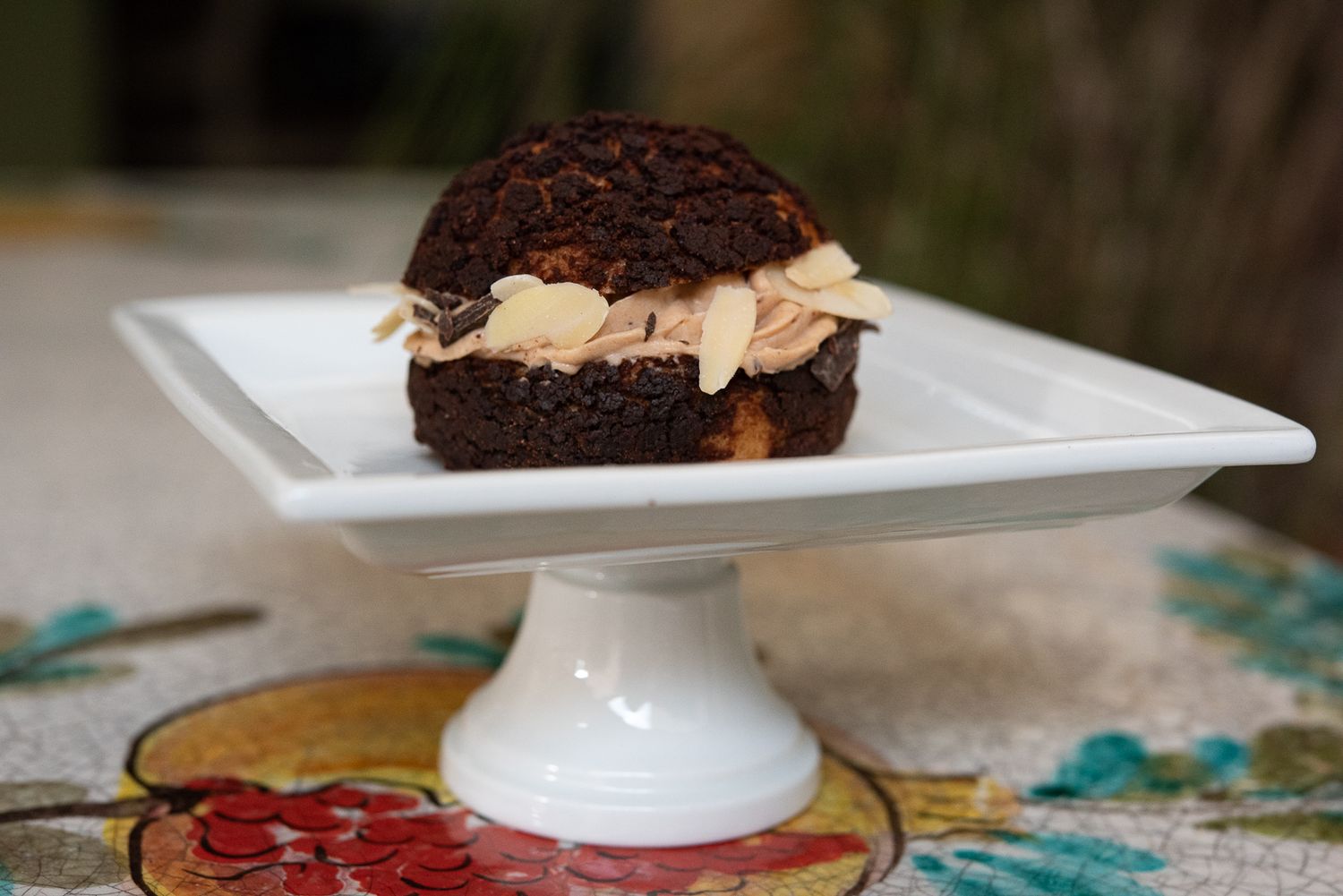 An assortment of chocolate desserts and pastries displayed on white plates and cake stands on a floral tablecloth.