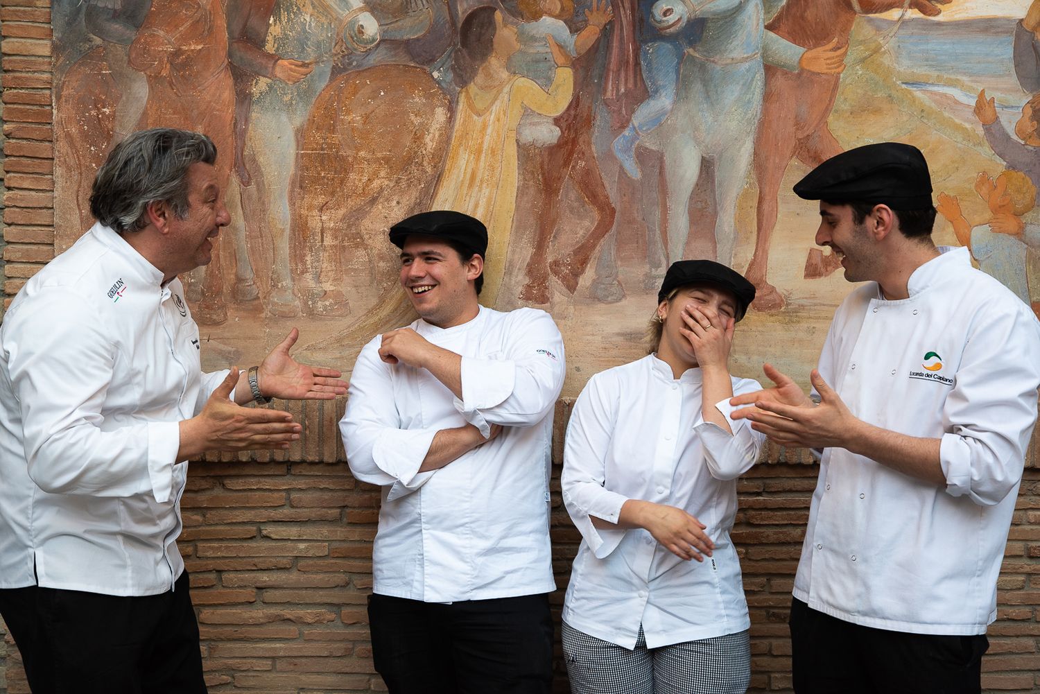 Chefs in white uniforms standing against rustic brick wall backdrop.