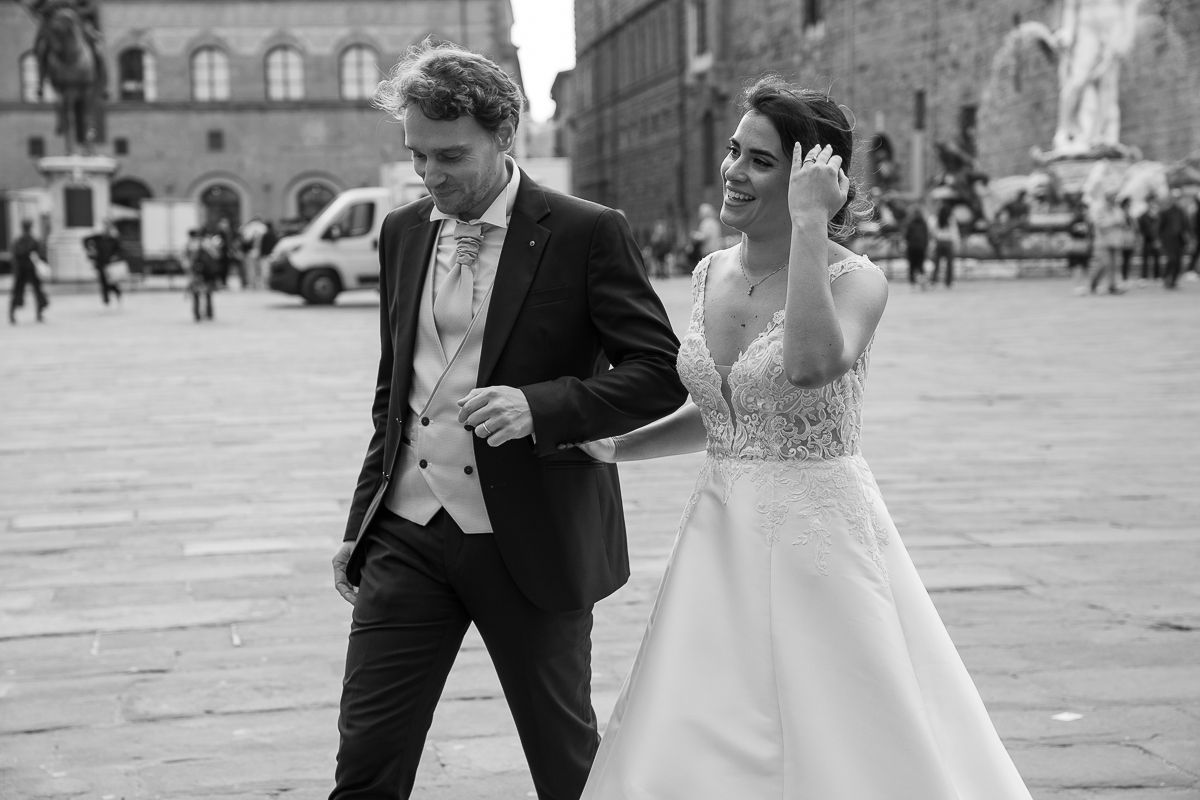 Black and white photo of a bride and groom walking in a European plaza on their wedding day.