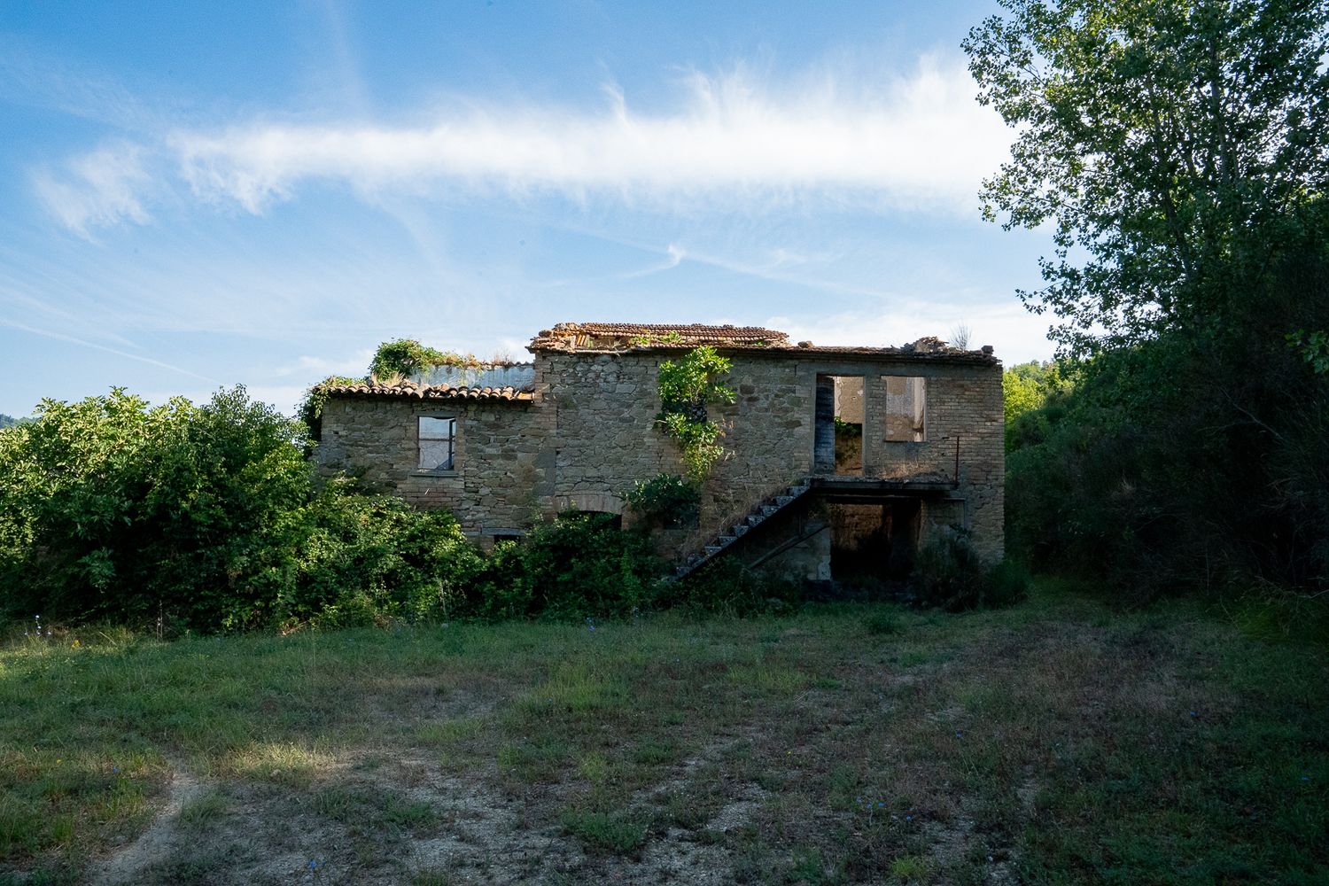 Abandoned stone farmhouse with deteriorating walls set against bright blue sky.