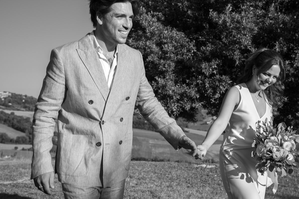 Black and white photo of a couple holding hands outdoors, rolling hills behind on their elopement day in Umbria shot by Friderika Wollweber.
