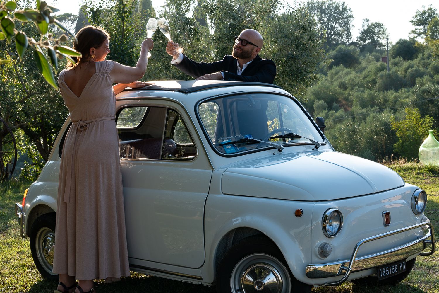 Classic white Fiat 500 parked in a sunny vineyard setting with scenic rural landscape in the background.