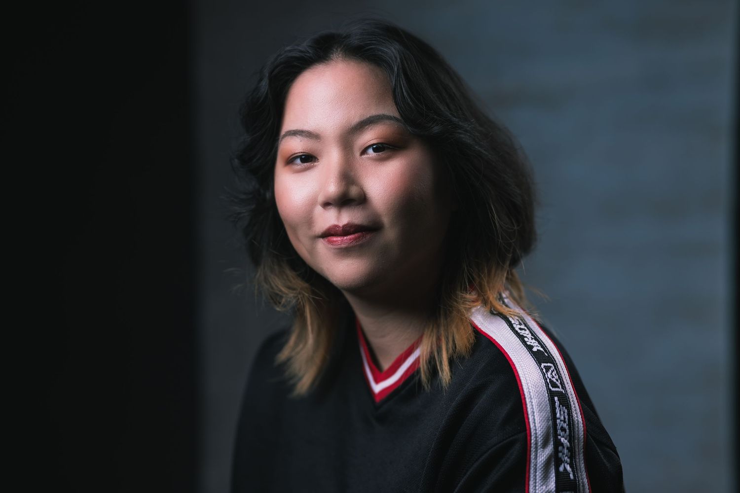 Side-lit studio portrait of person in black athletic jersey with striped sleeves.