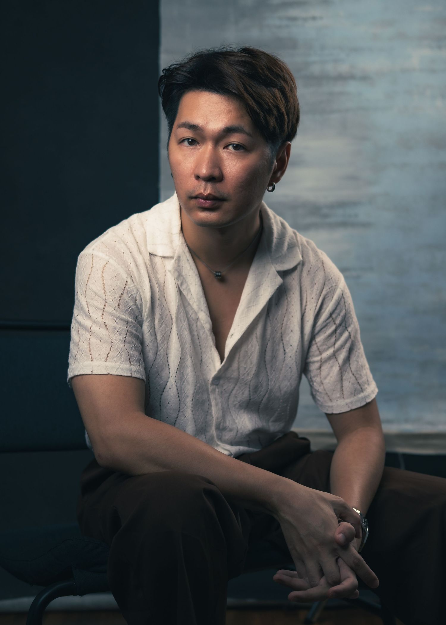 Person in white button-up shirt poses thoughtfully in moody studio lighting.