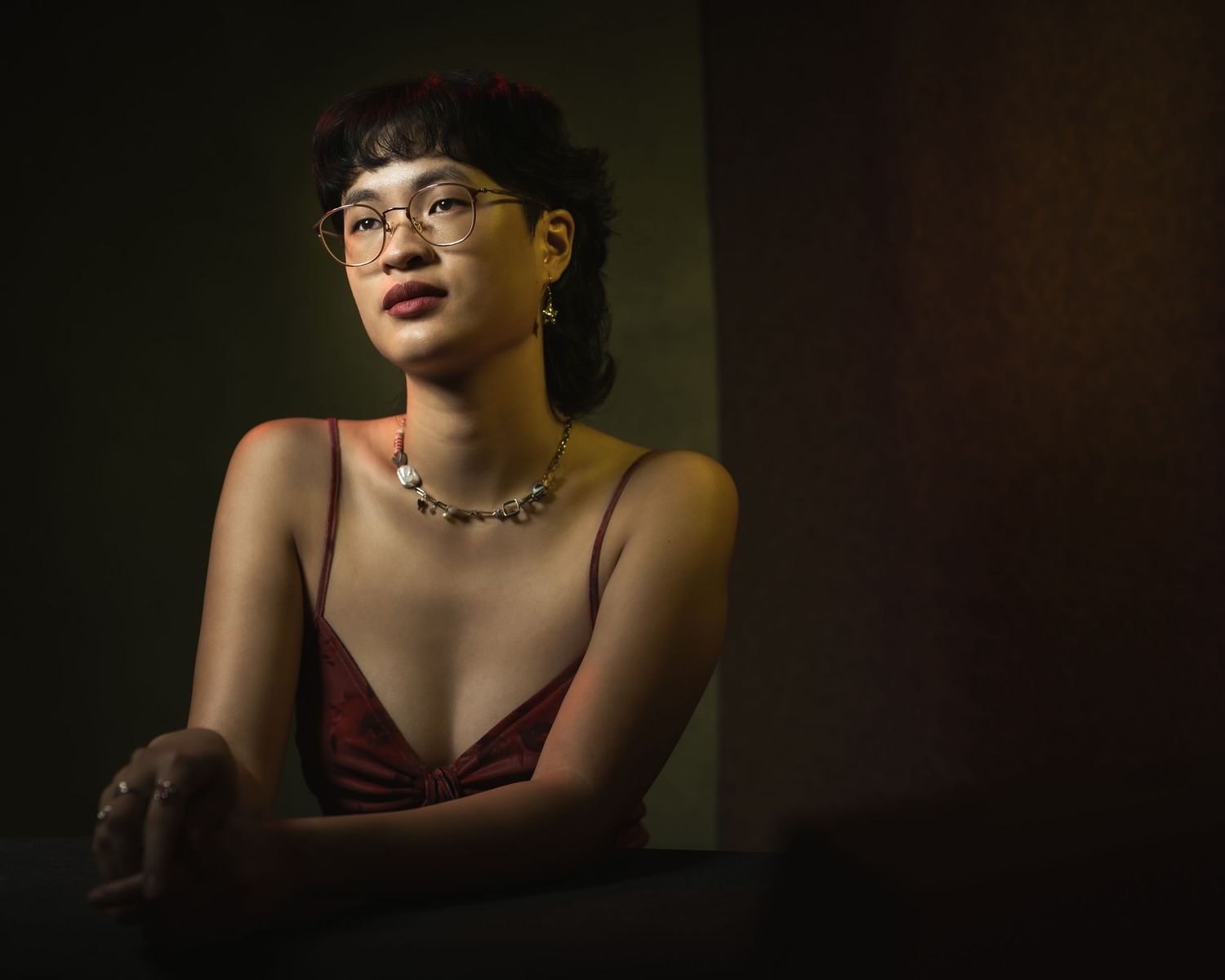 A dramatic series of portraits in dark lighting shows someone in burgundy clothing against a shadowy background.